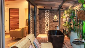A modern outdoor seating area with a stone wall, a black bathtub, and potted plants. - Exōtico Beach Hotel (Cahuita)