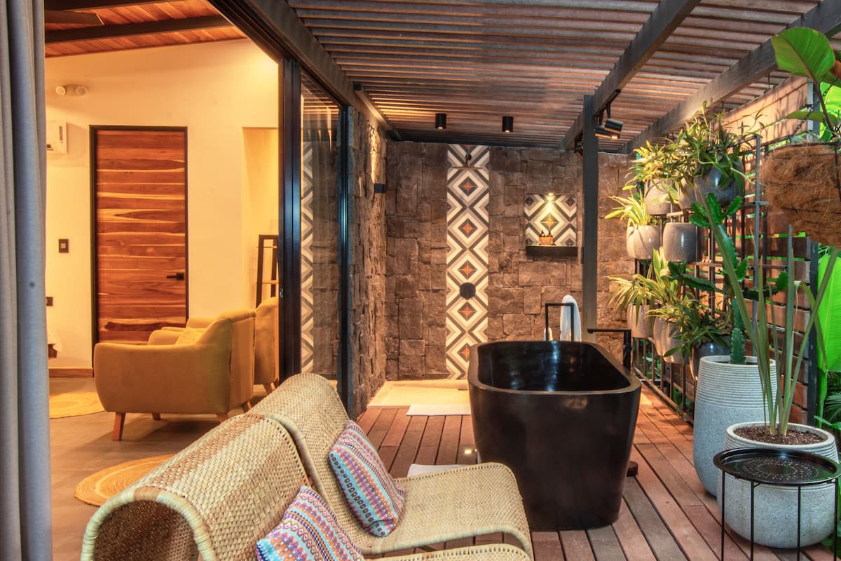 Un área de estar moderna al aire libre con una pared de piedra, una bañera negra y plantas en macetas.