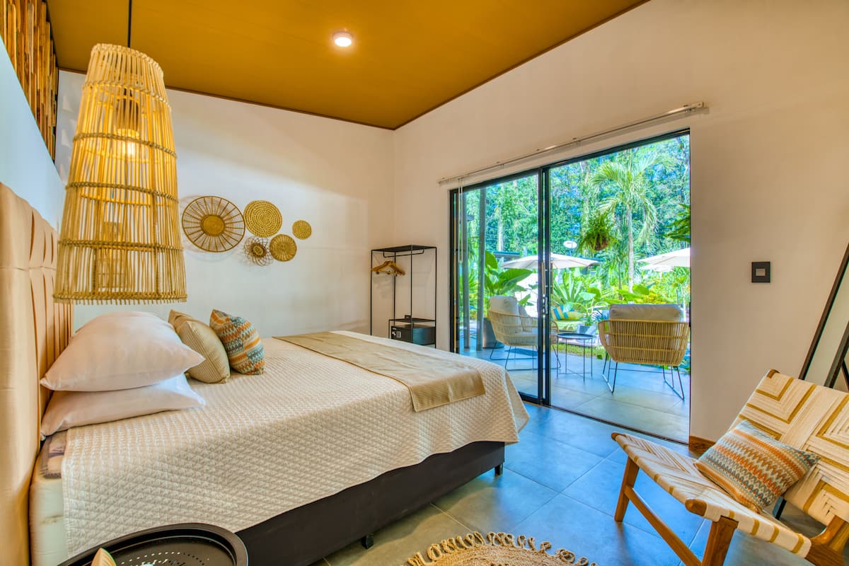 Un dormitorio con cama, mesita de noche y vistas a un área exterior con sillas y sombrillas.