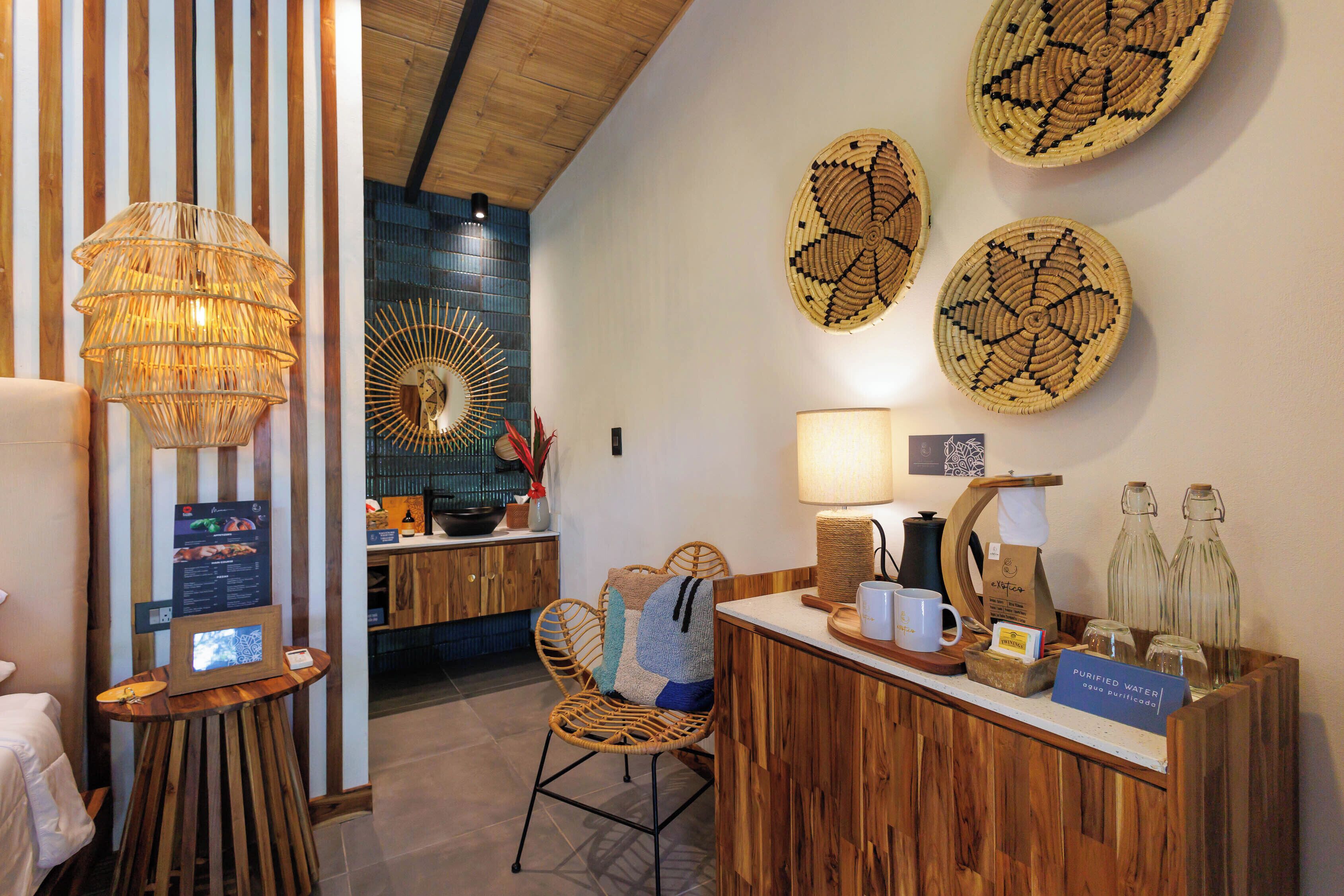 Un espace d’accueil comprenant un comptoir de réception en bois, un fauteuil en osier, une lampe fixée au mur et des assiettes décoratives en fibres tressées.