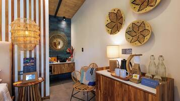Un espace d’accueil comprenant un comptoir de réception en bois, un fauteuil en osier, une lampe fixée au mur et des assiettes décoratives en fibres tressées.