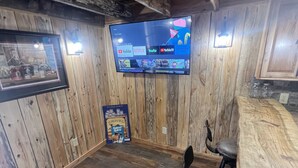 Una habitación con paneles de madera, un televisor con aplicaciones de streaming, un cuadro enmarcado y una zona de bar.