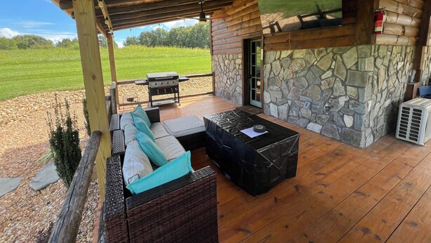 Un espacio de estar al aire libre cubierto con pared de piedra, una parrilla y un televisor.