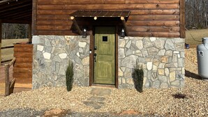 Una cabaña de madera con cimientos de piedra, una puerta verde y una ventana pequeña.