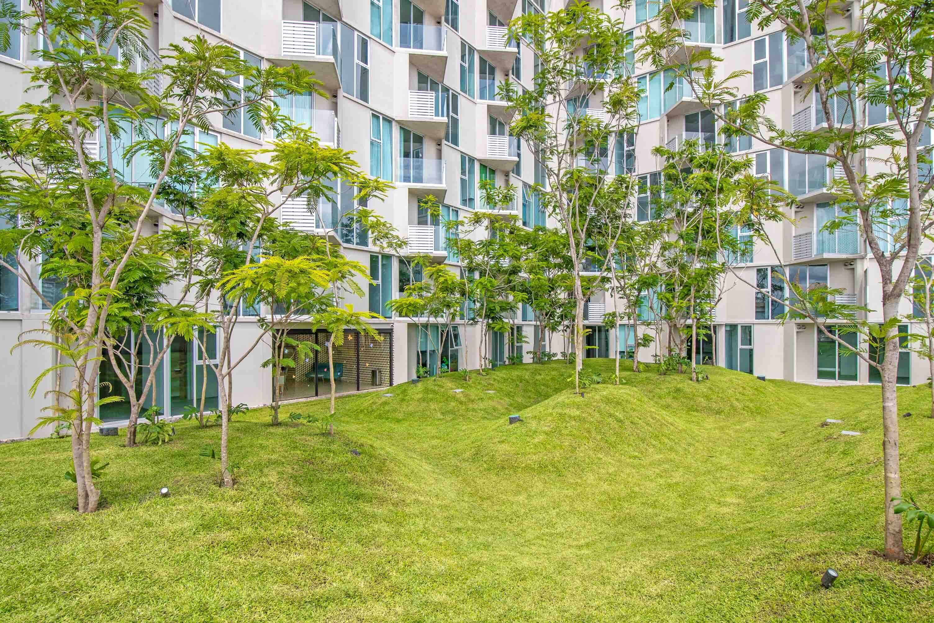 Um edifício de apartamentos moderno, com várias varandas e uma área ajardinada com árvores jovens.