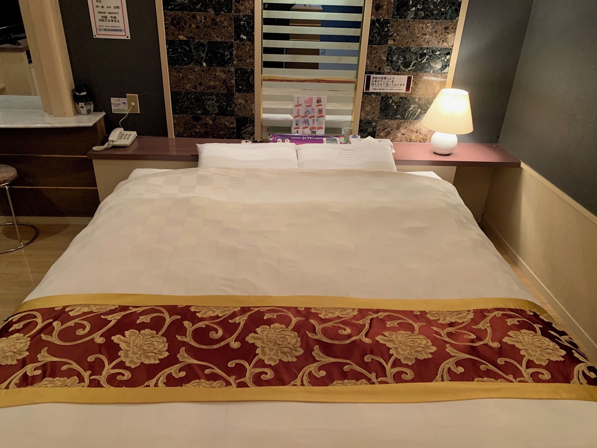 Una habitación de hotel con una cama, un escritorio con lámpara, un teléfono y un espejo.
