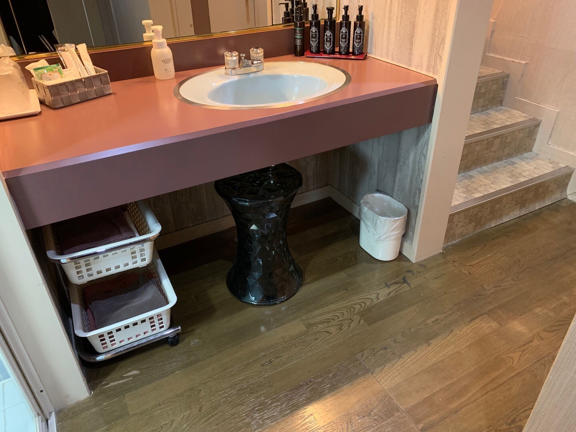 Une salle de bain avec un lavabo en marbre, des articles de toilette, une poubelle et un panier de rangement.