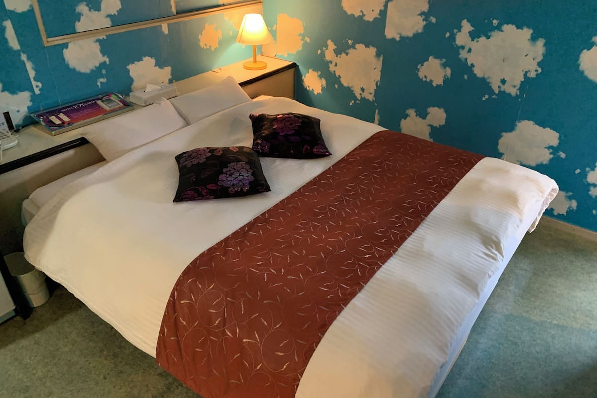 A hotel room with a bed, pillows, a nightstand, a lamp, and a wall with a blue and white pattern.