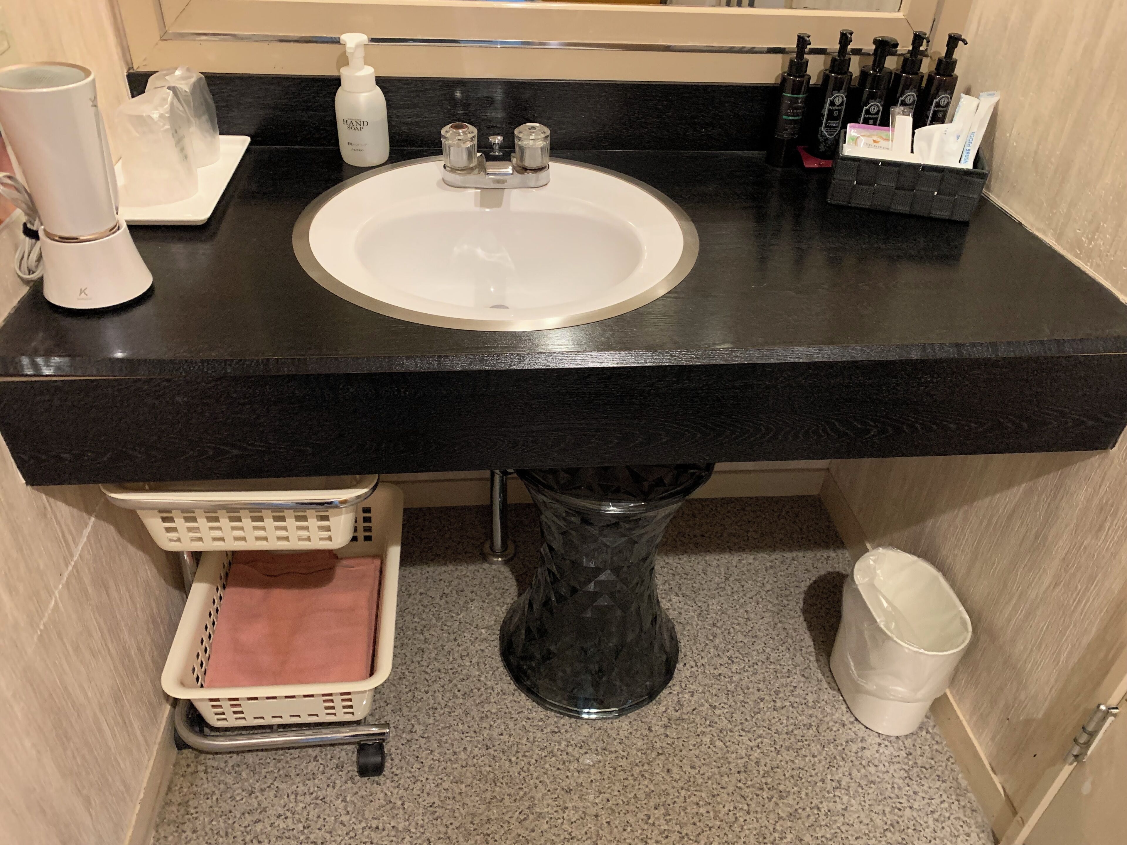 A bathroom with a black countertop, a white sink, a hand soap dispenser, and a bottle of hand sanitizer.