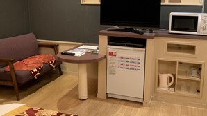 Un espacio habitable compacto con un sofá, una mesita con un control remoto, un refrigerador, un microondas y un televisor.