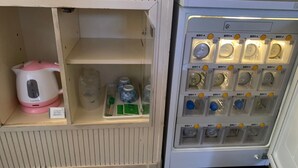 Un módulo de almacenamiento con estantes que contienen una tetera rosa, un recipiente blanco y varias botellas.