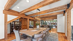 A spacious dining area with a wooden table and chairs, a chandelier, and a view of the kitchen in the background. - Carpe Montem - Modern, Views, Large Deck, Hot Tub, Private (Sundance)