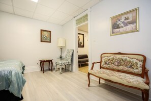A room with a bed, a chair, a sofa, and a lamp. There are paintings on the walls.