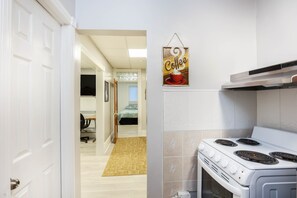 A kitchen with a white stove, a coffee sign, and a hallway leading to a bedroom.