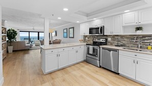 Una cocina moderna con armarios blancos, electrodomésticos de acero inoxidable y vistas al exterior.