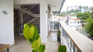 Un balcón amplio con vistas a una zona residencial, una escalera que conduce a un piso superior y una planta en maceta en primer plano.