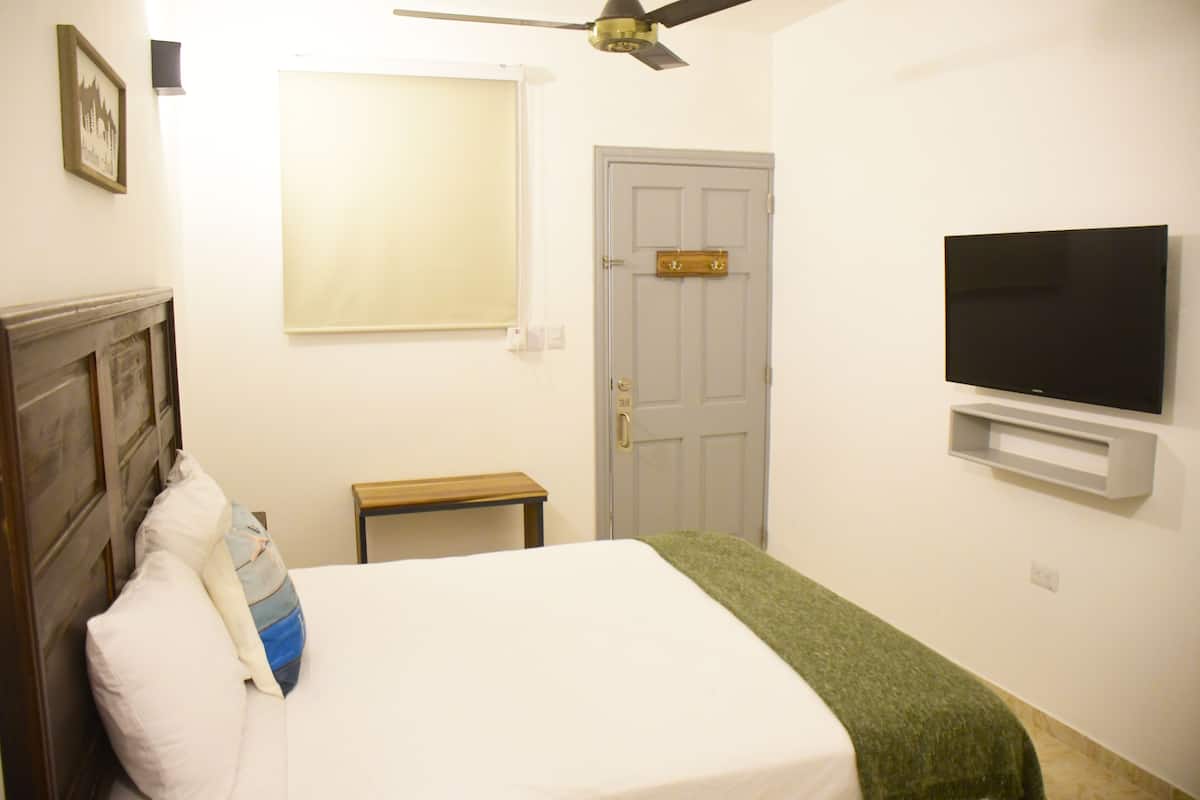 A bedroom with a bed, a television mounted on the wall, a door, and a window.