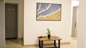 Un pasillo con una obra de arte enmarcadas de una ola, una mesita con una planta, y una puerta con manija.