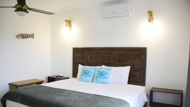 Una cama bien tendida con un cabecero de madera, dos mesitas de noche y un ventilador de techo.