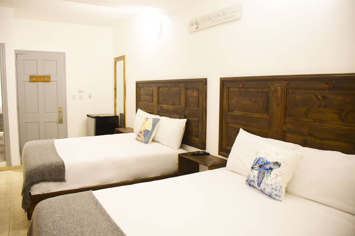 A hotel room with two single beds, wooden headboards, white bedding, and a small bedside table with a lamp.