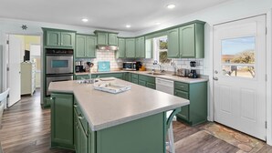 A modern kitchen with green cabinets, stainless steel appliances, and a large island.