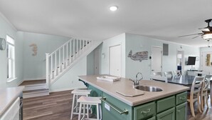A modern kitchen with a central island, white bar stools, and a dining area with chairs.