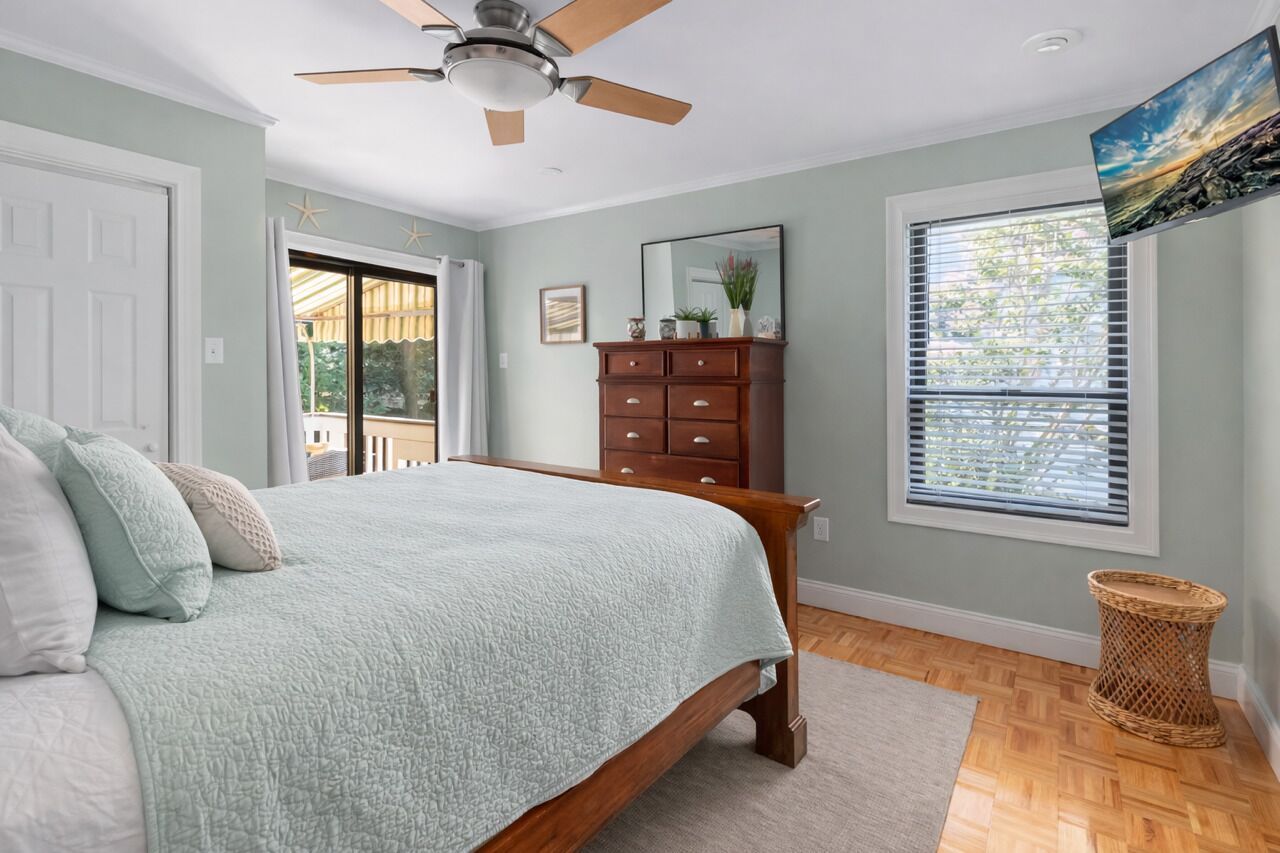 Un dormitorio con cama, ventilador de techo, cómoda, ventana con persianas y puerta que da a un área exterior.