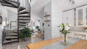 A modern kitchen with white cabinets, a wooden dining table, and a spiral staircase. - Water Views - 3 Min Walk to Private Beach - Luxury 5-Star Rated Beach House (Lower Township)