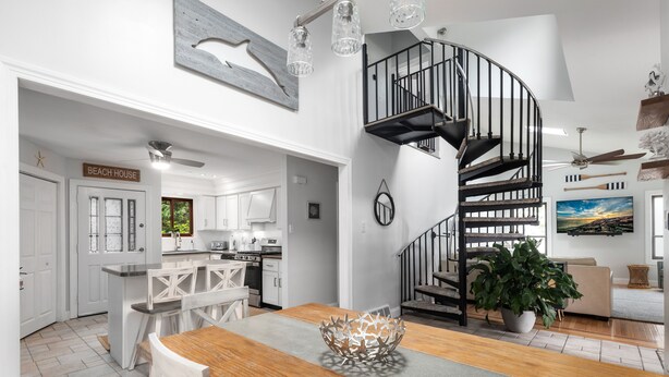 A modern kitchen with white cabinetry, a wooden dining table, and a black spiral staircase. - Water Views - 3 Min Walk to Private Beach - Luxury 5-Star Rated Beach House (Lower Township)