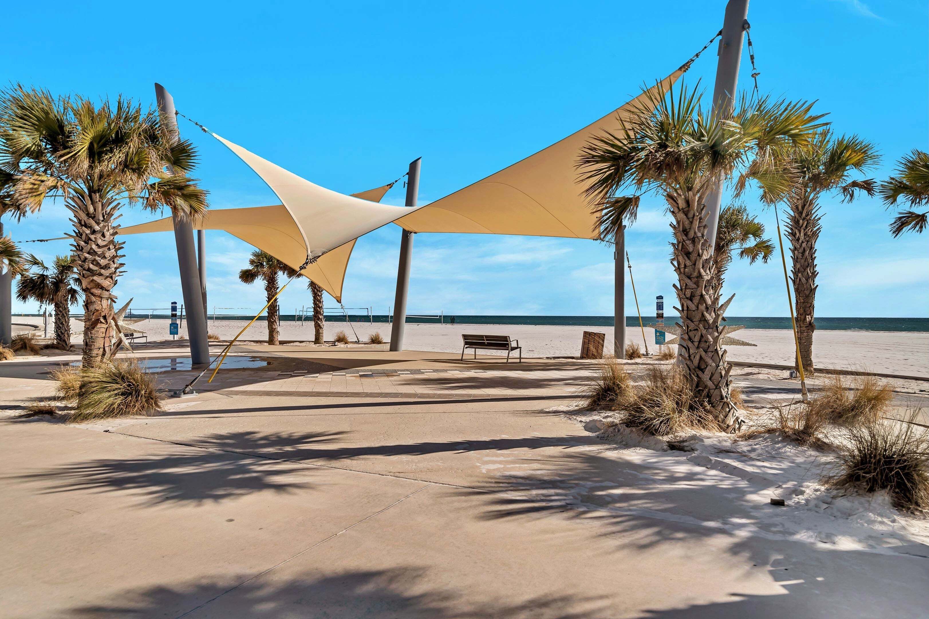 A beachside area with palm trees, a bench, and a large shade structure.