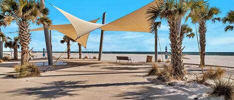 A beachside area with palm trees, a bench, and a large shade structure.