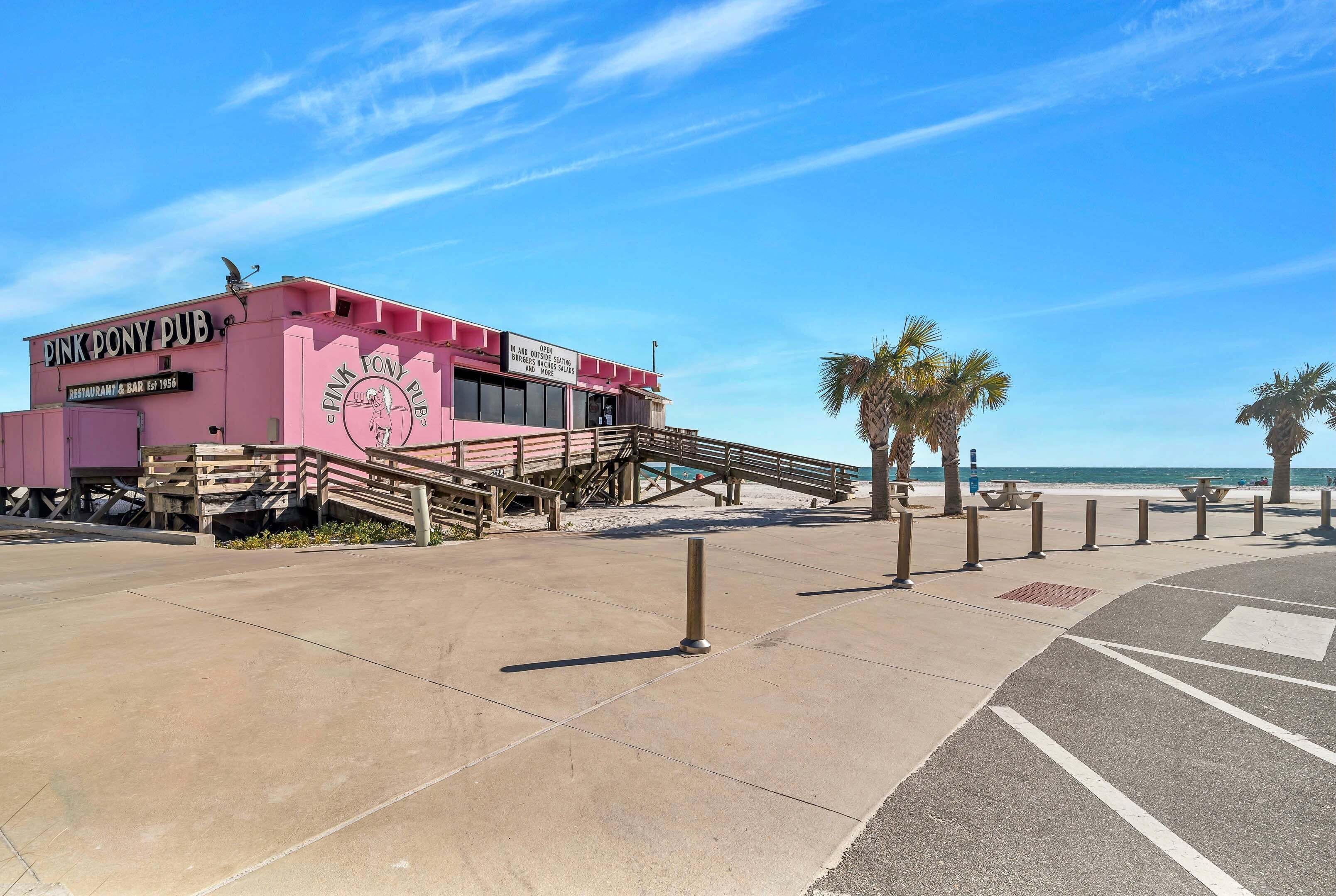 A pink building with a sign reading 'Pink Pony Pub,' a staircase, and a beach in the background.