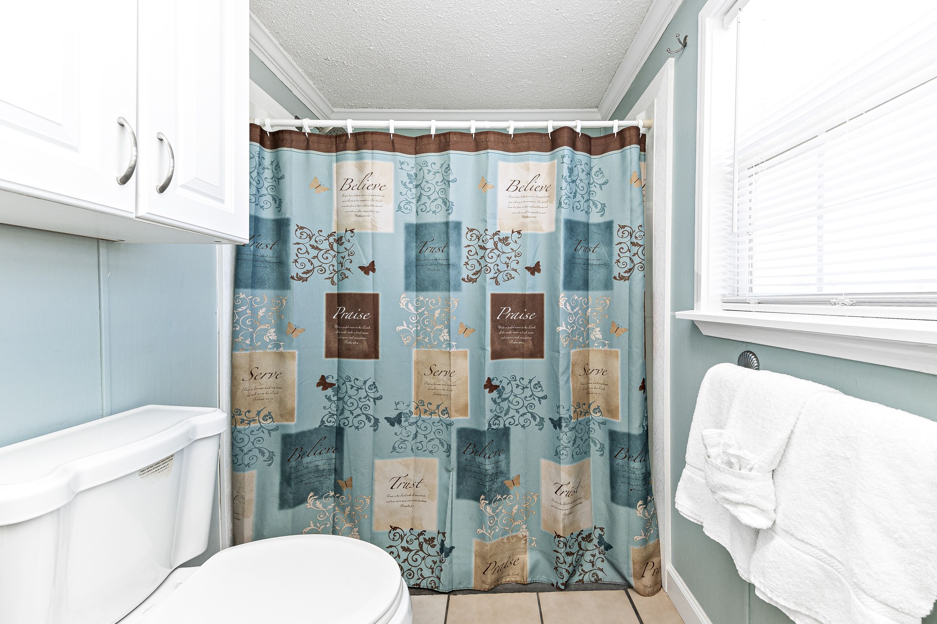 Une salle de bain équipée d’un rideau de douche orné de phrases motivantes, de toilettes et d’un porte-serviettes.