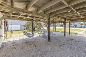 An outdoor covered area with wooden beams, a swing set, and picnic tables.