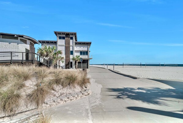 A beachfront property with a curved building, a concrete pathway, and a sandy beach.