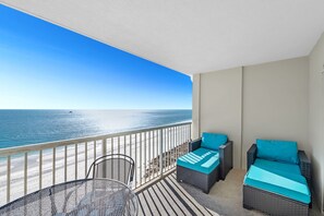 A balcony with a view of the ocean, wicker furniture, and a metal table.