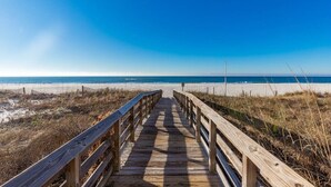 A wooden boardwalk leading to a beach with a clear blue sky.