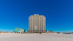 A tall hotel with multiple balconies, a beach in the foreground, and a clear blue sky.