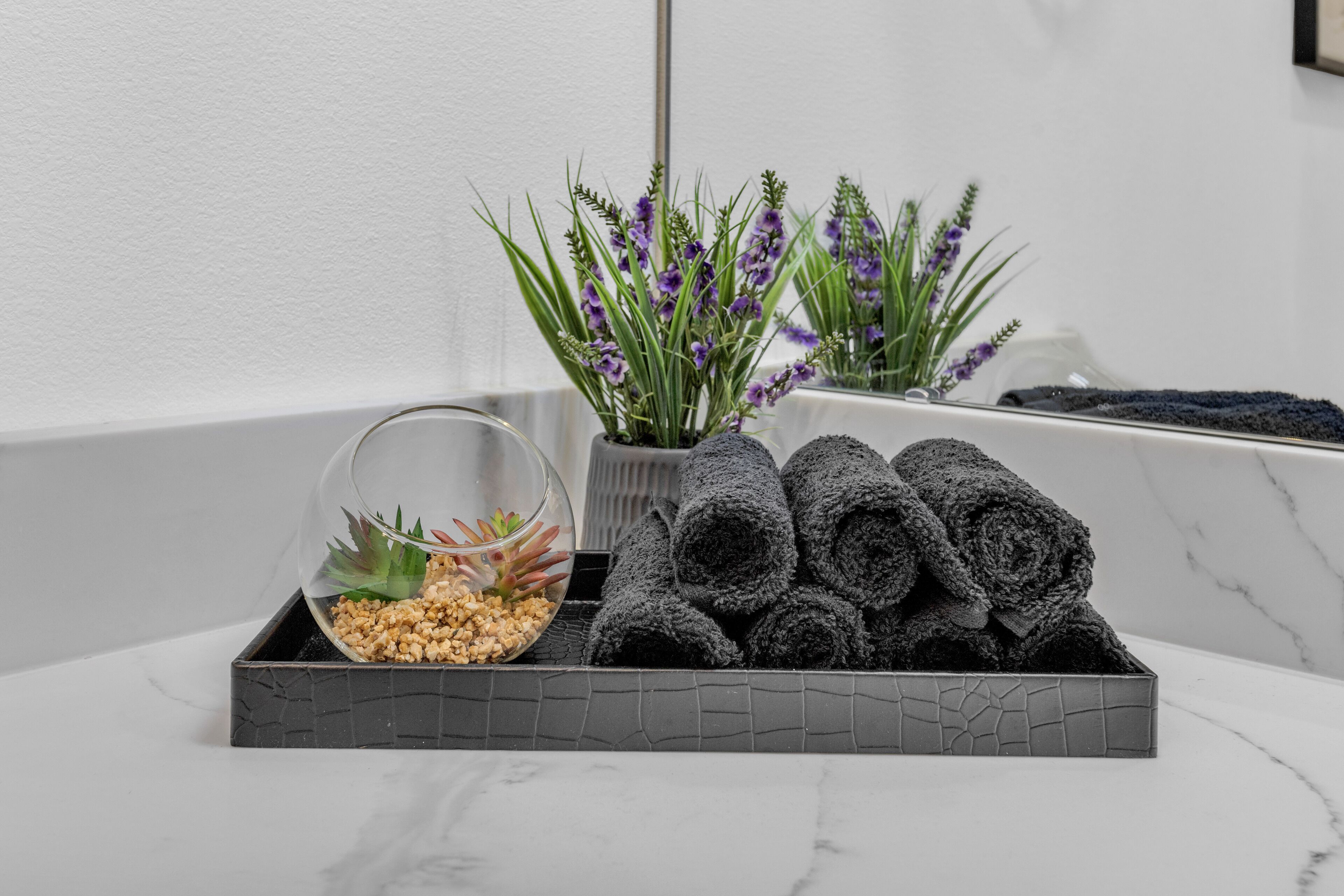 A bathroom with a marble countertop, a glass bowl with a plant, and rolled towels.