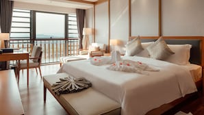 A hotel room with a large bed, a desk, a chair, and a view of the city through large windows. - White Swan Guest House Meizhou (Meizhou)