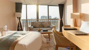 A hotel room with a bed, a desk with a laptop, a sofa, and a view of the city through large windows. - White Swan Guest House Meizhou (Meizhou)
