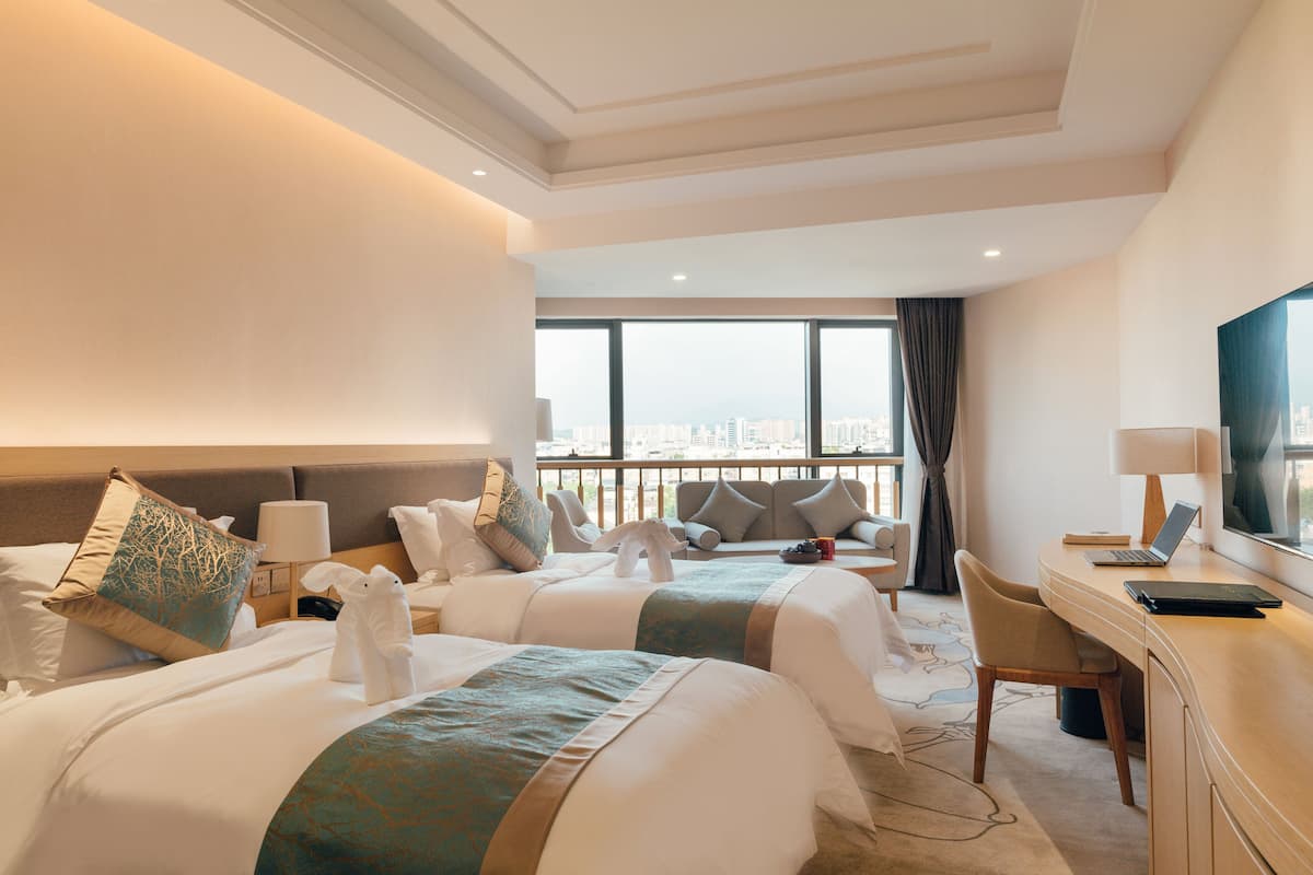 Habitación de hotel con dos camas, un escritorio, una silla, un televisor y un ventanal con vistas a la ciudad.