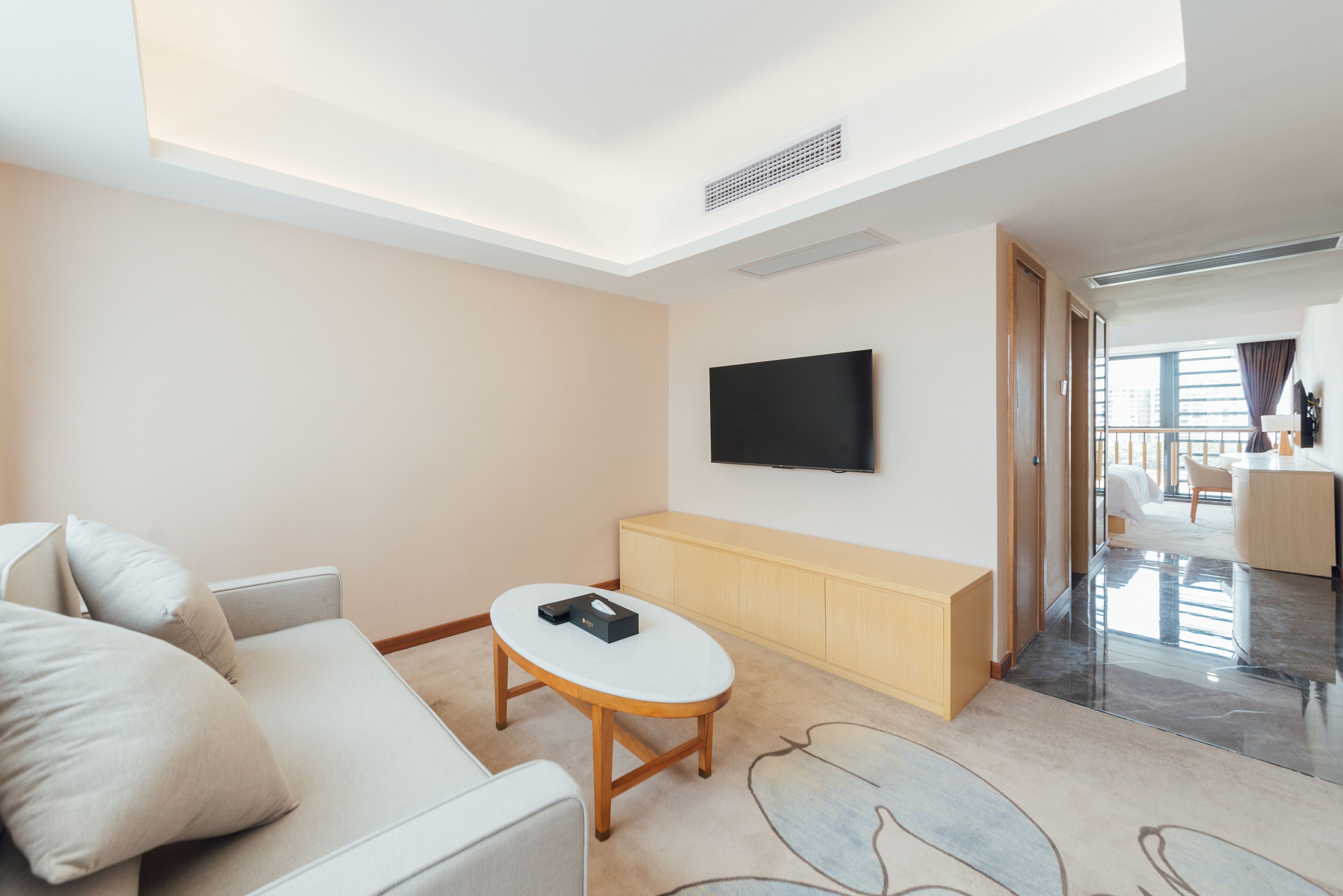 Une chambre d’hôtel moderne, équipée d’un canapé, d’une petite table, d’un téléviseur fixé au mur et offrant une vue sur le balcon.
