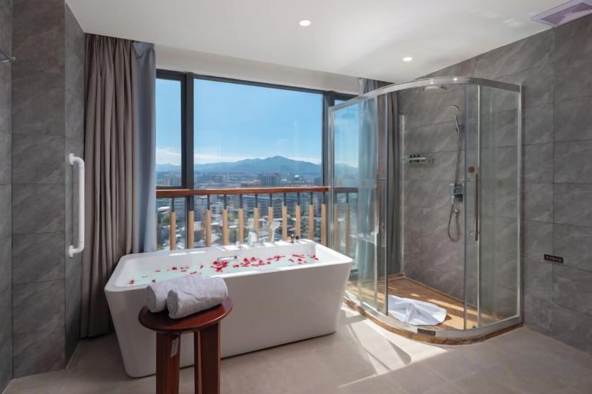 Ein modernes Badezimmer mit einer Glaskabine zur Dusche, einer freistehenden Badewanne und Blick auf eine Stadtlandschaft durch große Fenster.