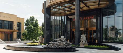 A modern hotel entrance with a curved canopy, a stone fountain, and two lion statues.
