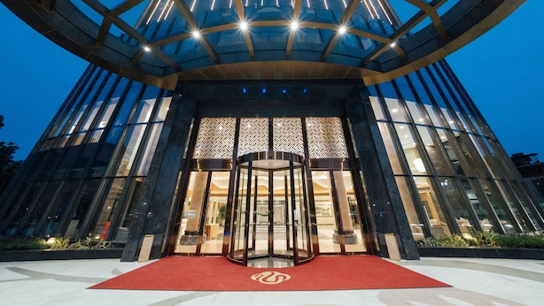 A modern hotel entrance with a revolving door, glass facade, and a red carpet leading to the entrance. - White Swan Guest House Meizhou (Meizhou)