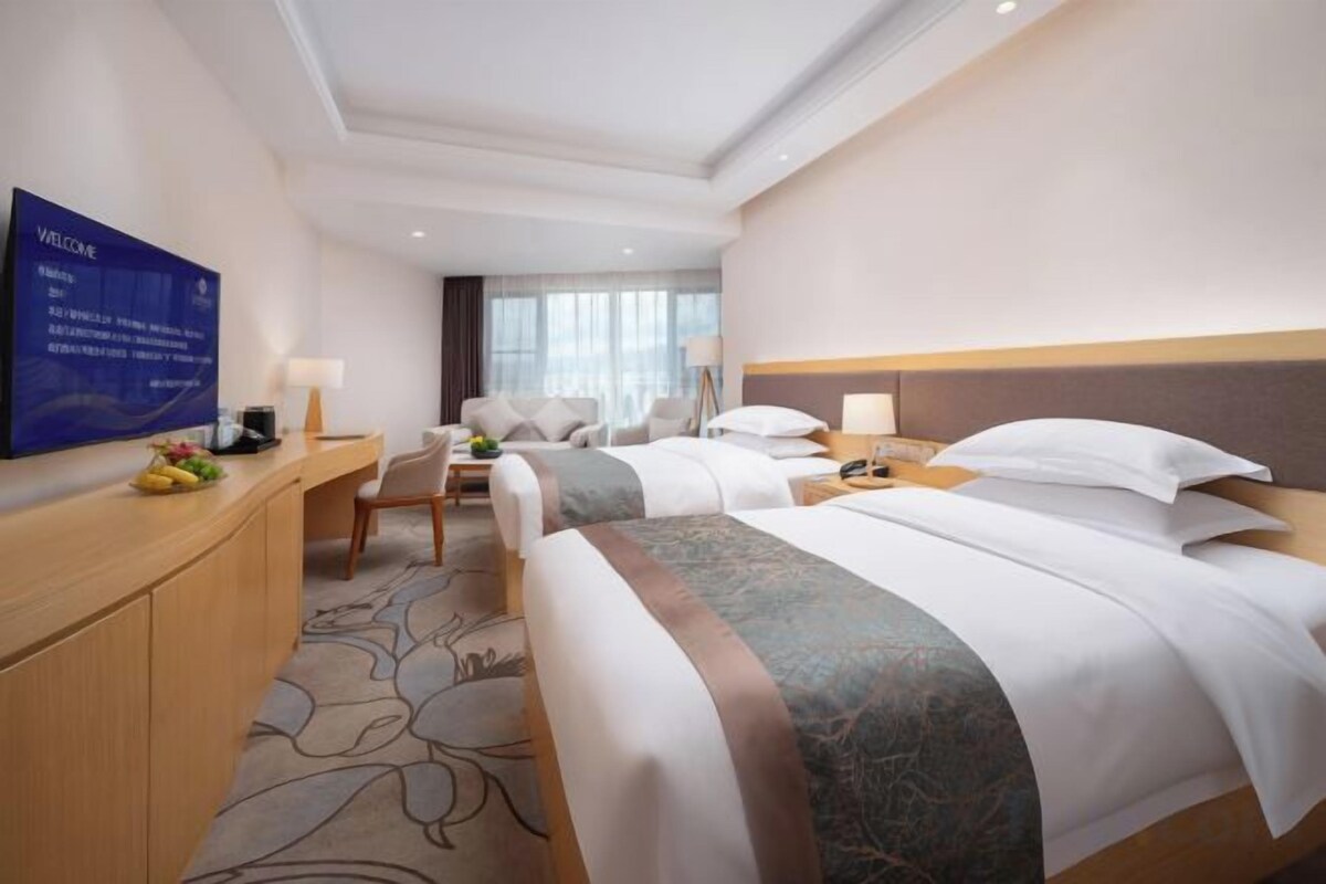Une chambre d’hôtel avec deux lits, un bureau, une télévision et une vue sur l’extérieur.