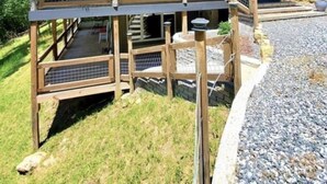 A two-story wooden cabin with a balcony, surrounded by trees and a gravel driveway. - Cozy cabin in Hot Springs, minutes away from town! (Hot Springs)