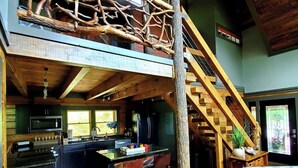 A rustic cabin interior with a loft bedroom, wooden floors, a kitchen with modern appliances, and a staircase. - Cozy cabin in Hot Springs, minutes away from town! (Hot Springs)