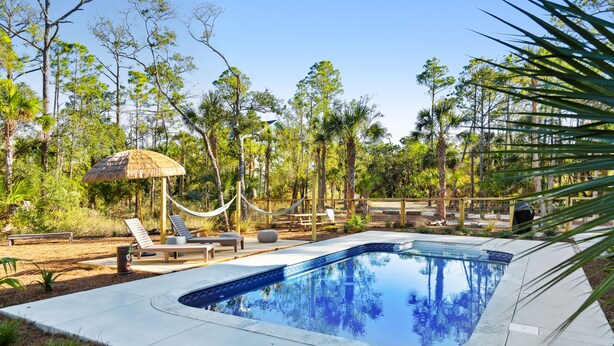 Una piscina con sillones de descanso y una hamaca, rodeada de árboles.